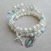 Swarovski ivory pearls are interspersed with crystal Paters and accents in crystal and aquamarine, with a sterling silver cross and Miraculous Medal.